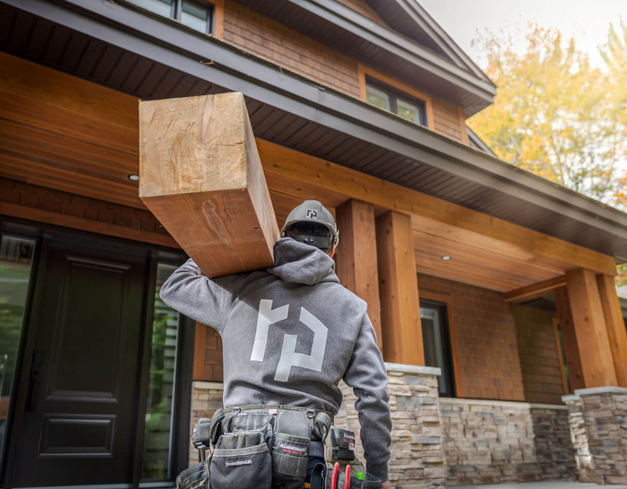 Ouvrier transportant bois en face d’une maison en bois